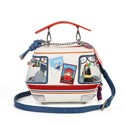 A whimsical handbag designed to look like a retro flying van, featuring a white body with red and blue stripes, clear window panels, a red top handle, a blue shoulder strap, and various cartoon character charms.