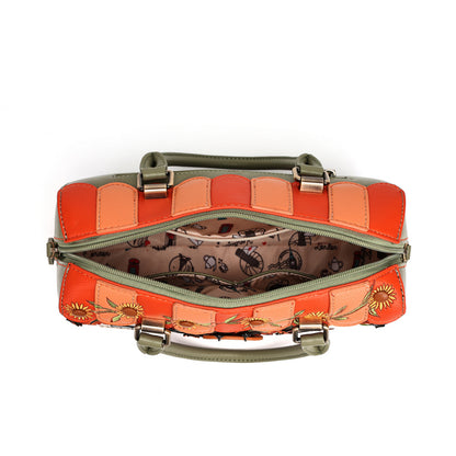 An open handbag with a patchwork exterior in orange, peach, and olive green, featuring floral embroidery on the front, a patterned interior lining, and top handles on a white background.