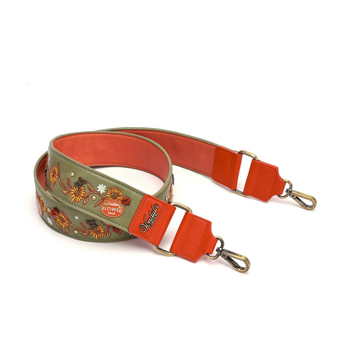 A wide, adjustable shoulder strap featuring a sage green outer fabric with colorful floral embroidery, a bright orange-red inner lining, and brass-toned metal hardware.