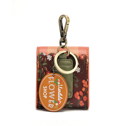 A small floral keychain wallet with a gold-tone clasp, a round key ring, and an oval hanging tag that reads 'Flower Shop' and 'Montilla'. The wallet has a dark red and orange floral pattern with green leaves and white daisy accents.