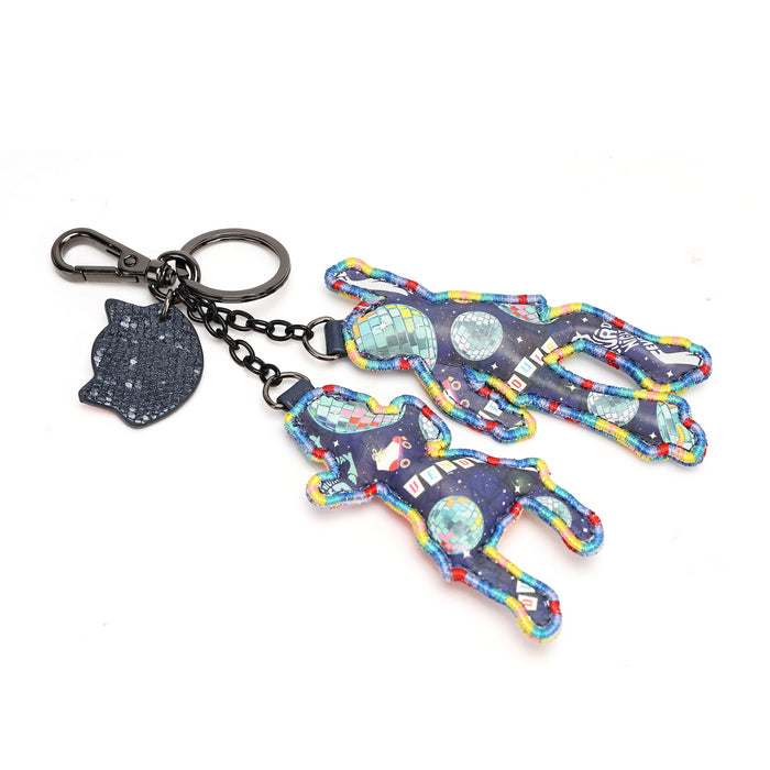 A keychain featuring three colorful astronaut-shaped fabric charms and a small textured cat-shaped tag, attached to a dark metal split ring and chain on a white background.