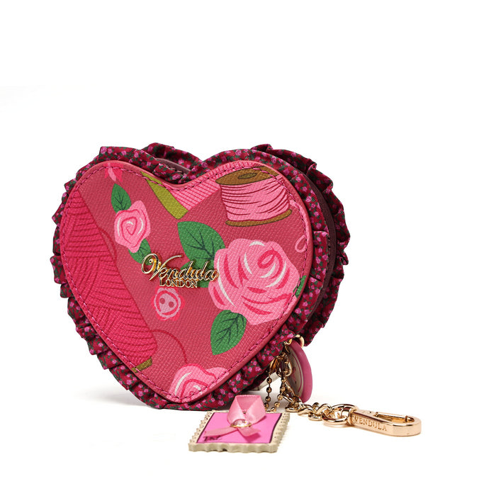 A heart-shaped pink fabric pouch with a floral rose pattern, featuring a ruffled dark pink border and a dangling gold-tone keychain charm with a pink bow, on a white background.