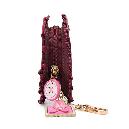 A burgundy faux-leather coin purse with a ruffled edge, featuring a pink and white button charm and a pink bow keychain attached with gold-tone hardware, shown on a white background.