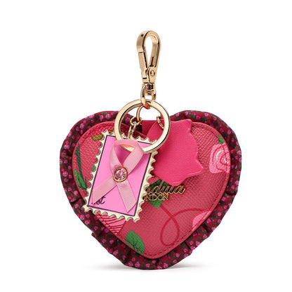 A heart-shaped pink and red floral keychain pouch with a gold-tone clasp, featuring a pink ribbon charm, a small stamp-shaped tag, and a gold-tone brand charm on a white background.