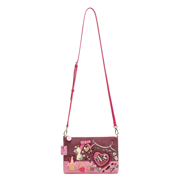 A pink crossbody bag with a long strap, decorated with various cartoon and fashion-themed patches, a heart-shaped charm, and a small pink pouch attached on the side, shown against a plain white background.