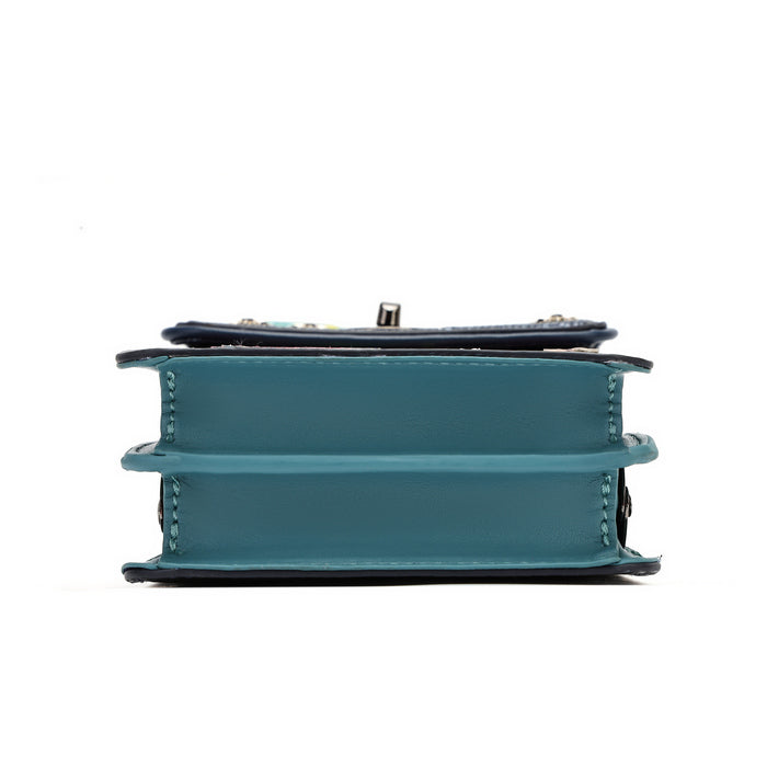 A teal blue faux-leather book-shaped clutch bag with a dark navy blue top flap and silver-tone hardware, shown from the side profile on a white background.