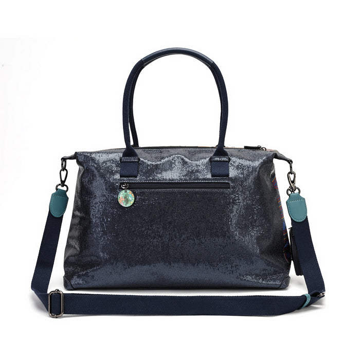 A navy blue sequined handbag with dark navy handles and a matching adjustable shoulder strap, featuring a small round decorative charm on the front pocket, set against a plain white background.