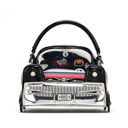 A miniature handbag designed in the shape of a classic car, featuring a glossy black body, a shiny chrome silver front grille, and a clear windshield showing colorful cartoon characters inside. It has a black handle and a license plate reading 'VENDU14'.