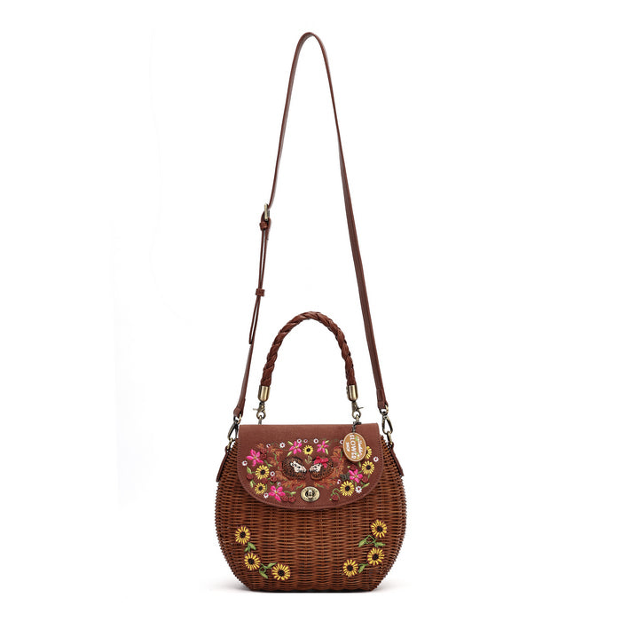 A brown woven wicker shoulder bag with a long shoulder strap, top handle, and floral embroidered details on the front flap and body, shown against a plain white background.