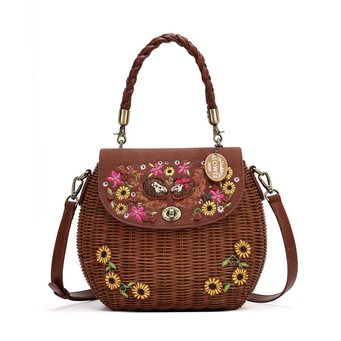 A brown woven wicker handbag with a braided top handle, a matching shoulder strap, and colorful floral embroidery on the front flap and lower body. A gold-tone metal tag on the front reads 'LOVE ITALY'.