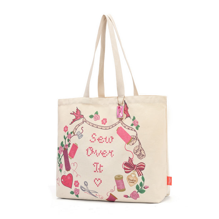 A cream canvas tote bag with long handles, decorated with a colorful 'Sew Over It' embroidery-themed graphic featuring pink, red, green, and purple details, set against a plain white background.