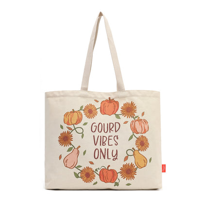 An off-white canvas tote bag with a printed autumn wreath design featuring pumpkins, sunflowers, pears, and the text 'GOULD VIBES ONLY' in brown, with beige handles and a small red tag on the side.