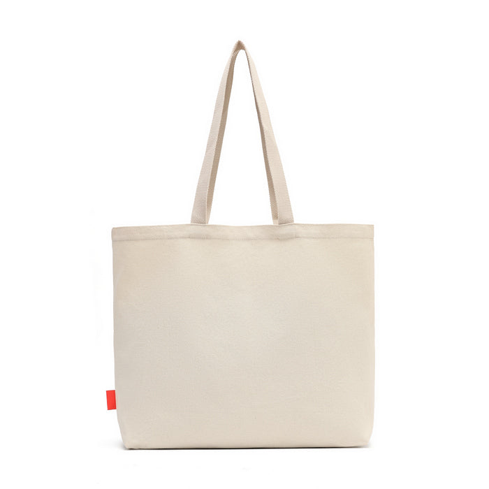 A light beige canvas tote bag with two shoulder straps and a small red fabric tag on the lower left side, shown against a plain white background.