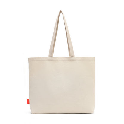 A light beige canvas tote bag with two shoulder straps and a small red fabric tag on the lower left side, shown against a plain white background.