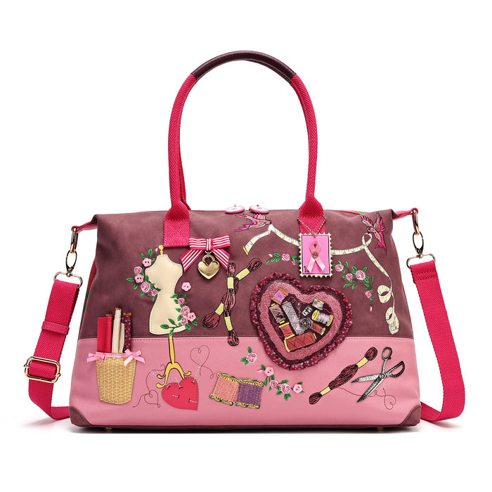 A roomy holdall for travel, busy days or carrying extra essentials, with twin handles and an adjustable detachable strap. The sewing-themed artwork combines cotton reels, ribbons, scissors and rose motifs with Pink Ribbon details, finished with hand-stitched accents.
