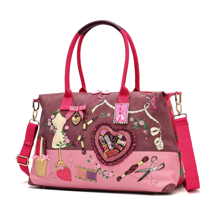 A roomy holdall for travel, busy days or carrying extra essentials, with twin handles and an adjustable detachable strap. The sewing-themed artwork combines cotton reels, ribbons, scissors and rose motifs with Pink Ribbon details, finished with hand-stitched accents.
