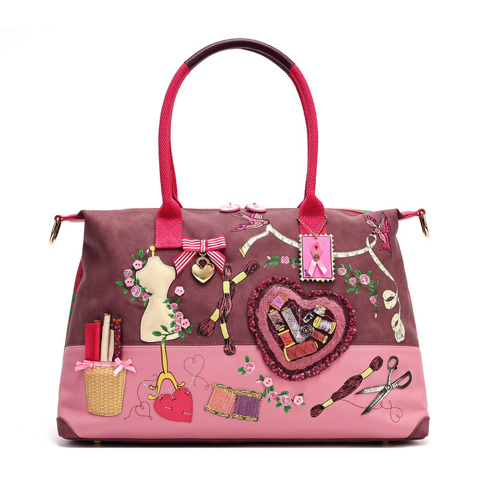 A roomy holdall for travel, busy days or carrying extra essentials, with twin handles and an adjustable detachable strap. The sewing-themed artwork combines cotton reels, ribbons, scissors and rose motifs with Pink Ribbon details, finished with hand-stitched accents.
