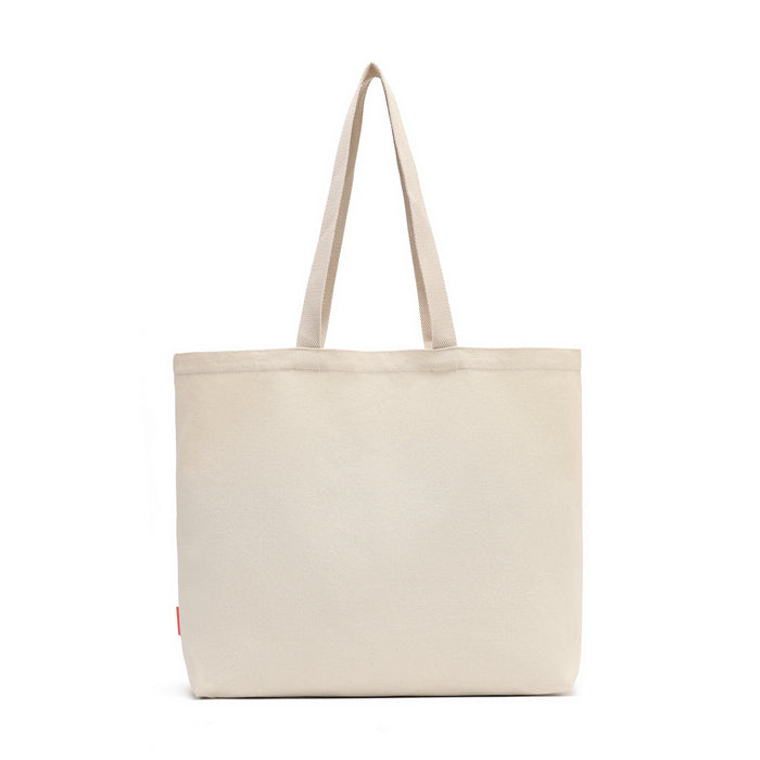 A plain canvas tote bag in a light beige or cream color, featuring two long shoulder straps and a small red tag on the lower left side, set against a solid white background.