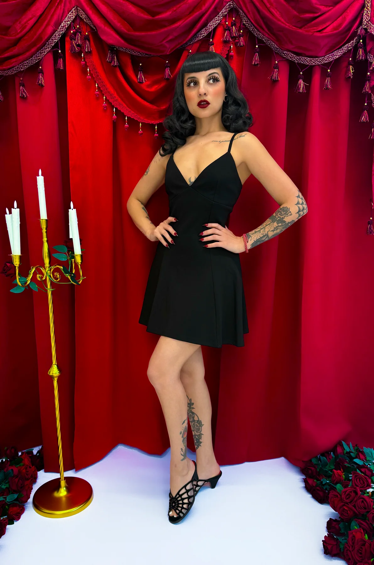 Woman in a black dress posing in front of a red curtain with decorative elements.