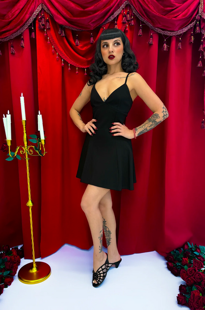 Woman in a black dress posing in front of a red curtain with decorative elements.