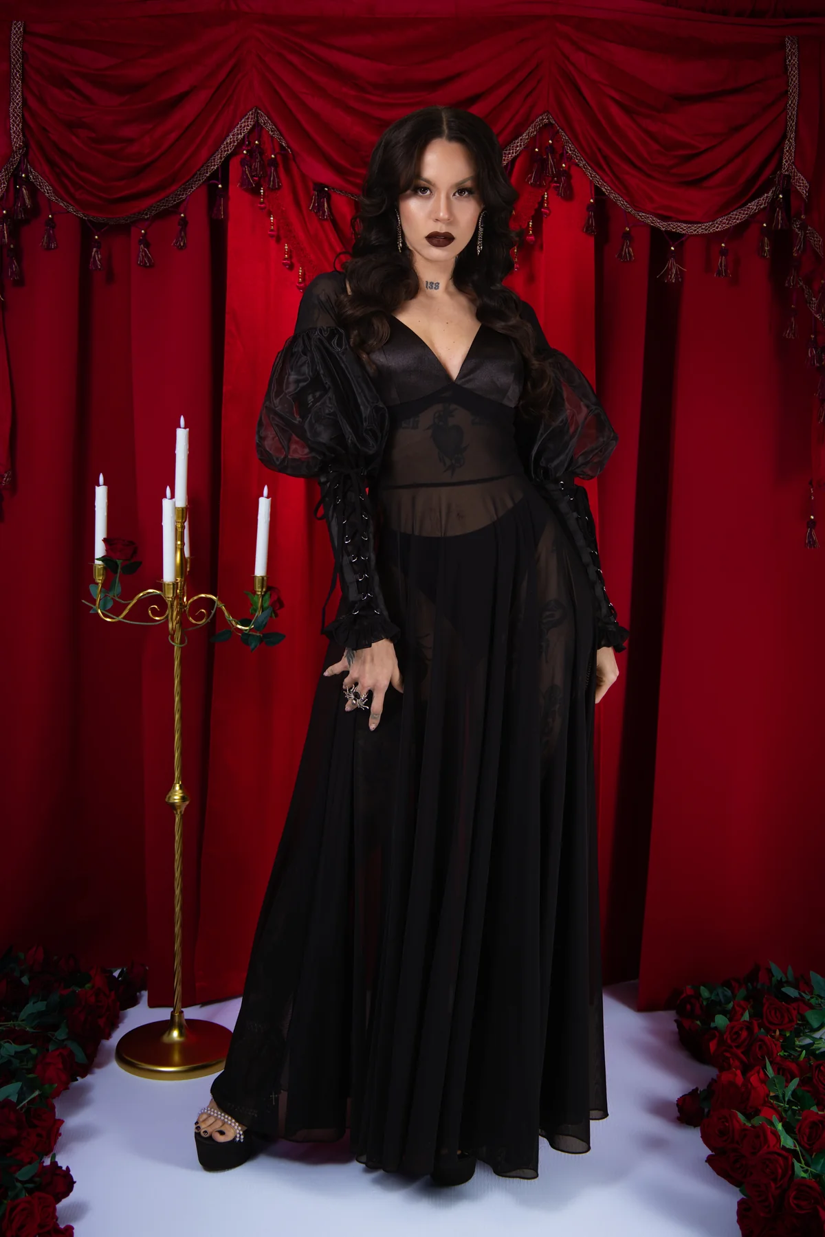 Woman in a black dress standing in front of red curtains with candles and floral decorations.