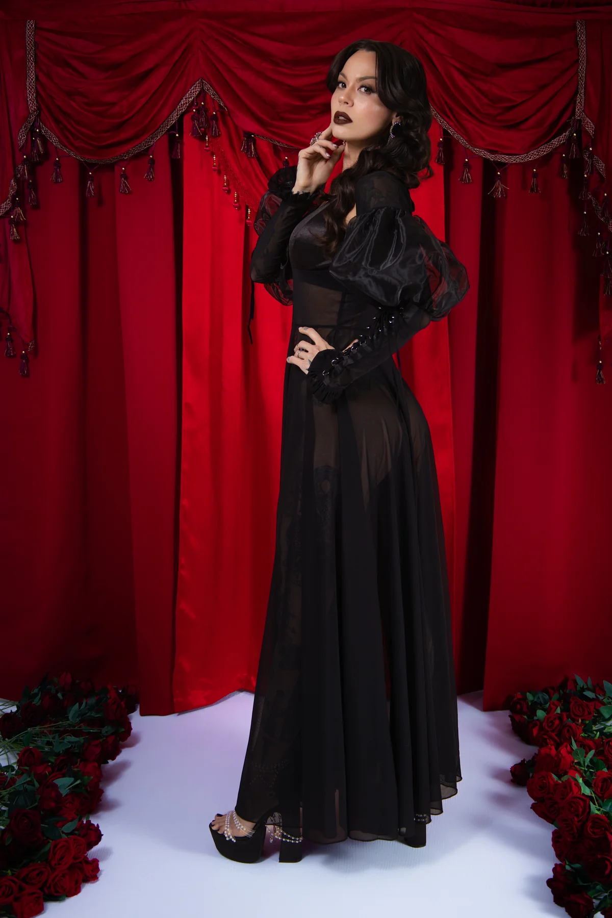 Woman in a black dress standing against a red curtain with floral decorations.