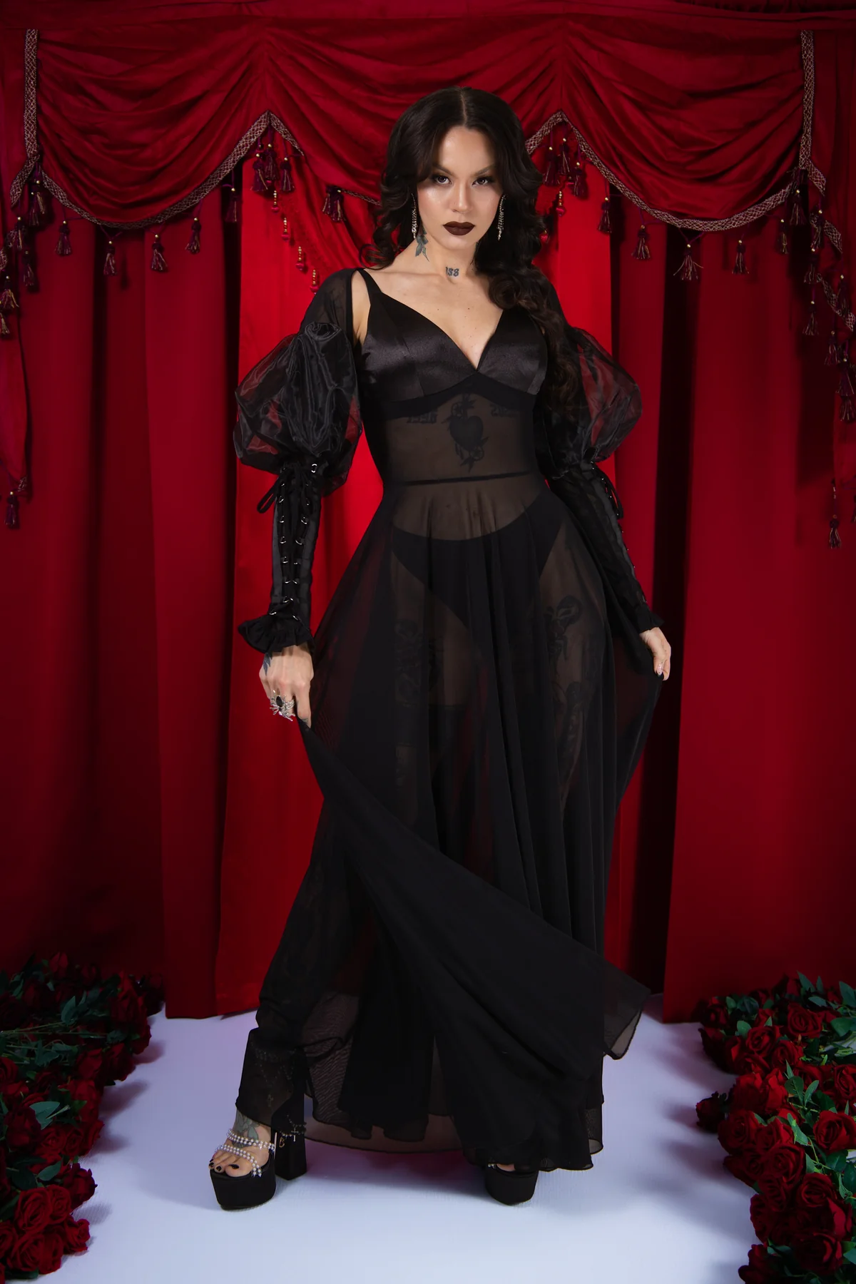 Woman in a black dress standing in front of red curtains with floral decorations.