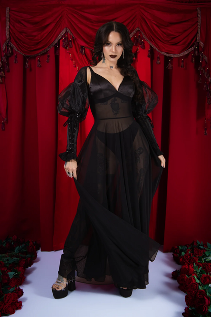 Woman in a black dress standing in front of red curtains with floral decorations.