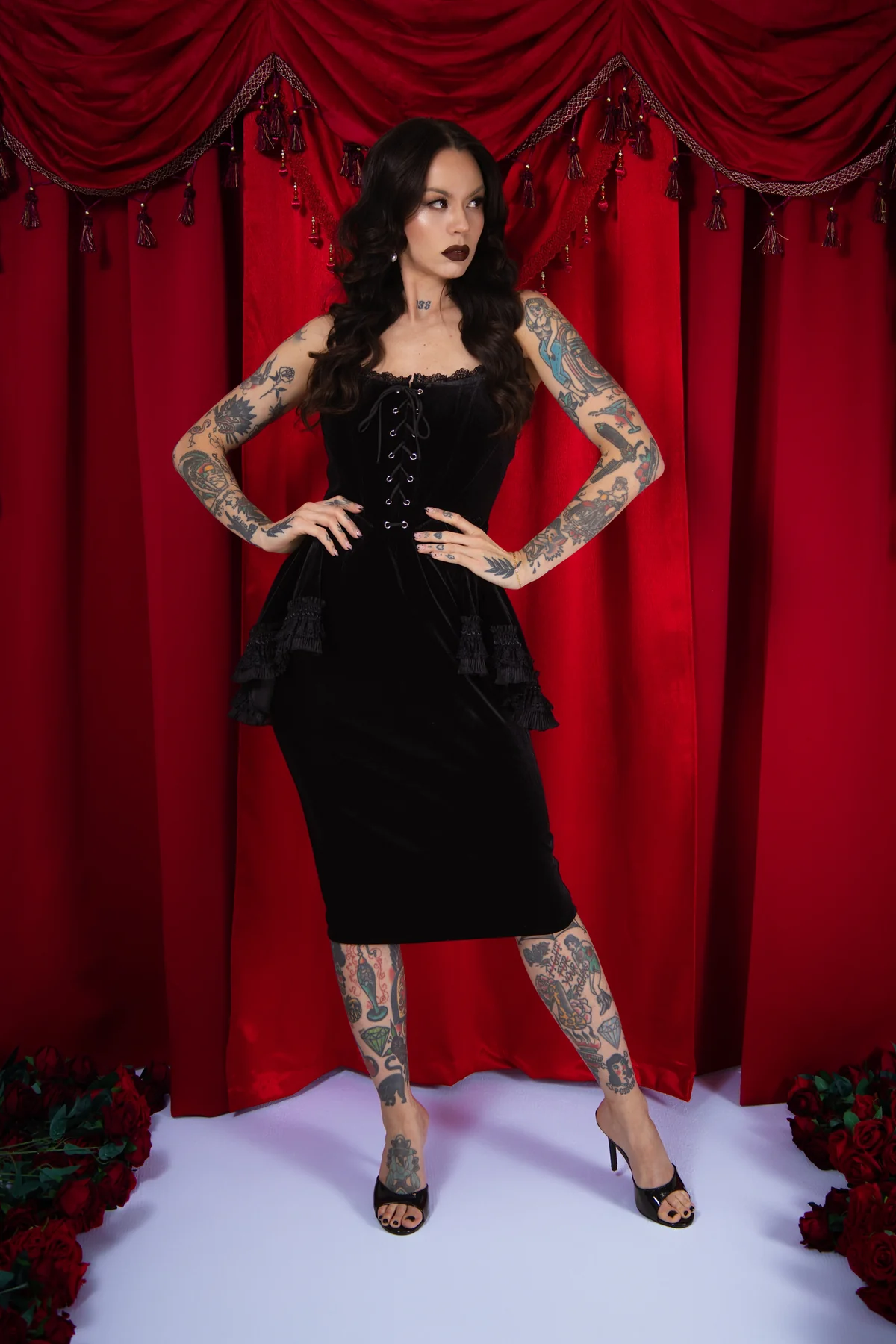 Woman in a black dress with tattoos standing in front of red curtains