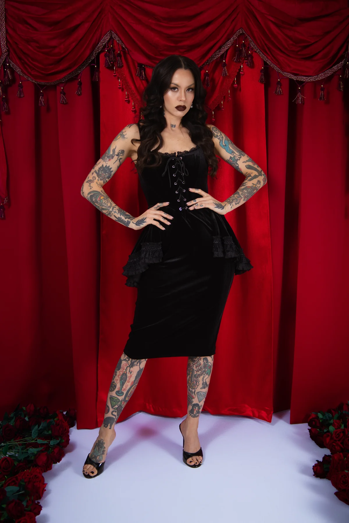 Woman in a black dress with tattoos standing in front of red curtains