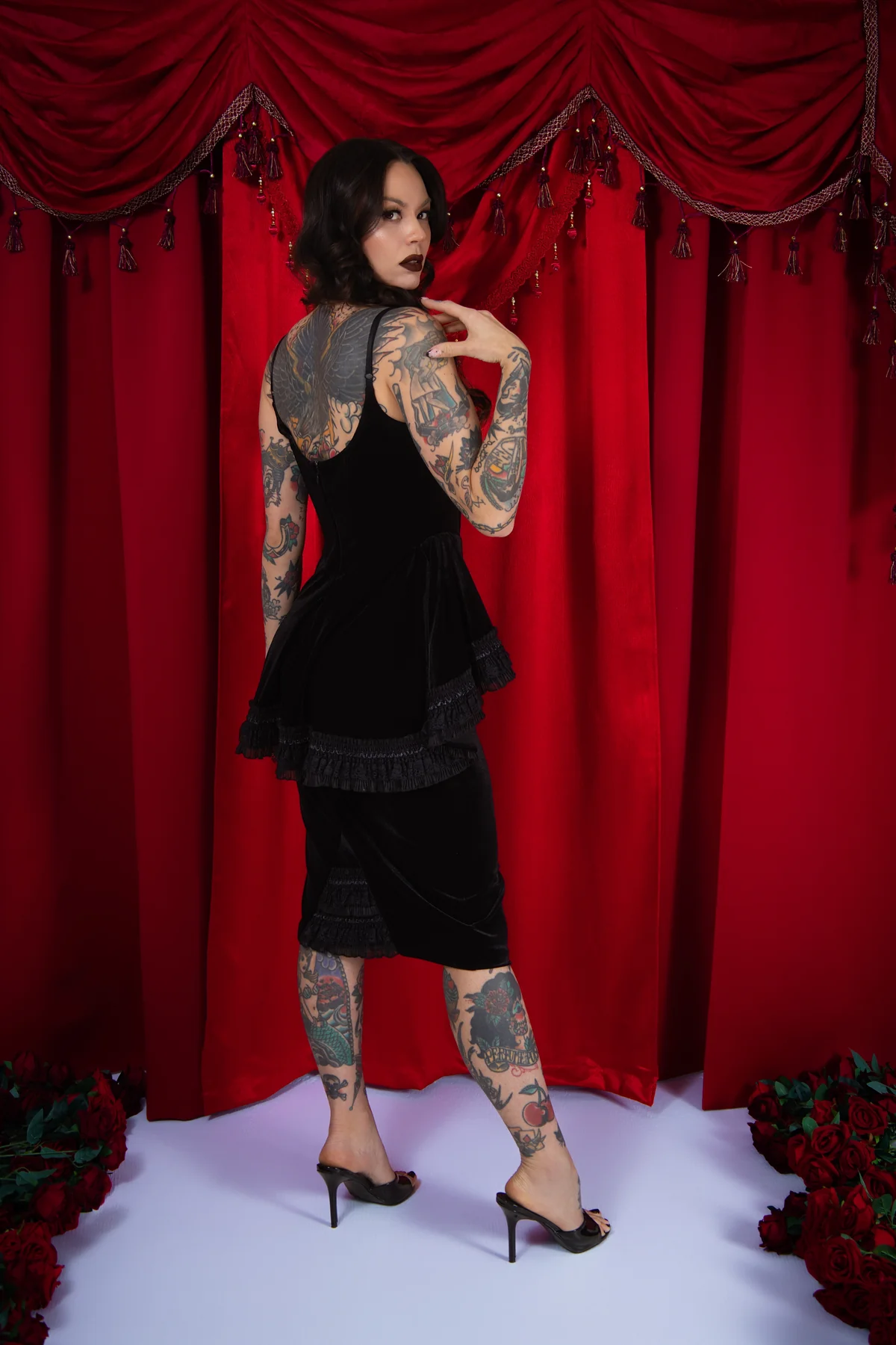 Woman in a black dress with tattoos standing in front of red curtains