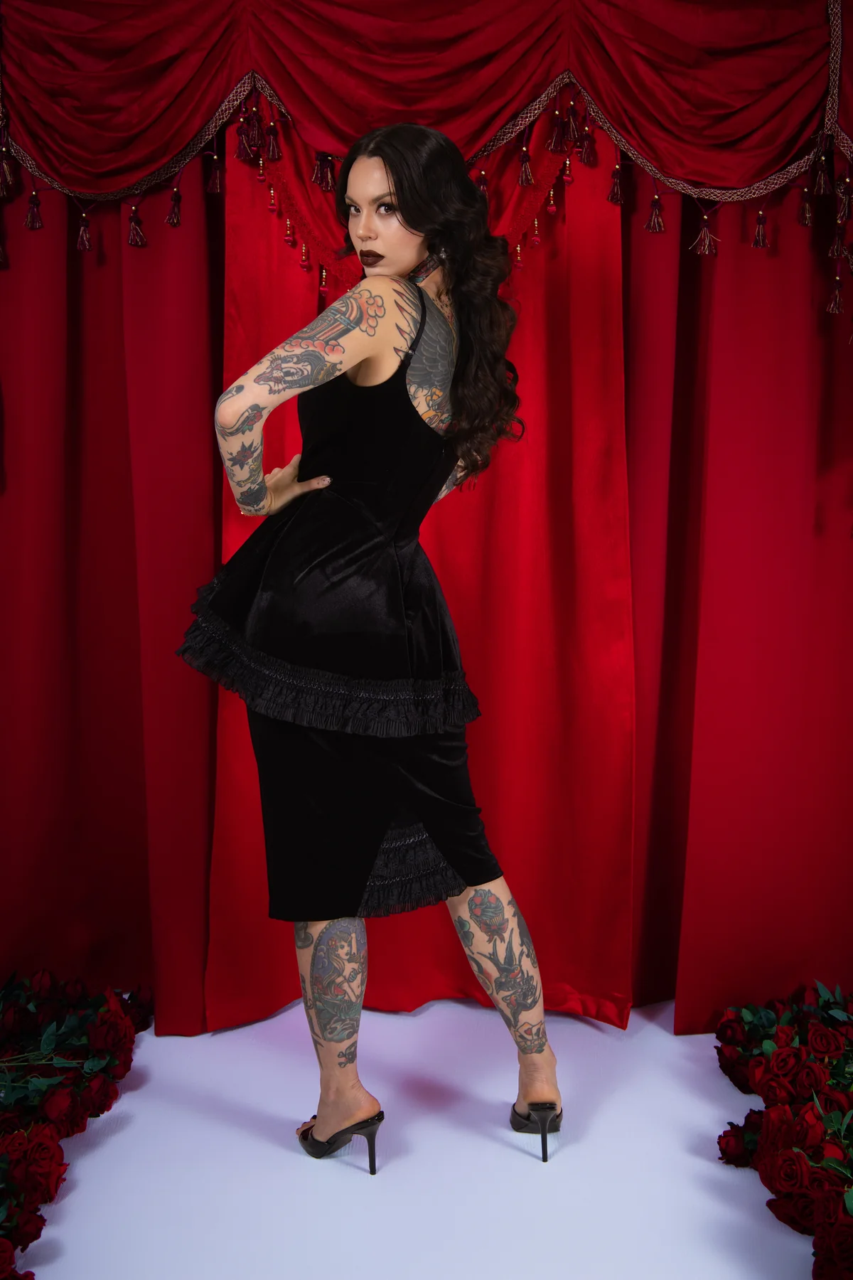 Woman in a black dress with tattoos standing in front of red curtains