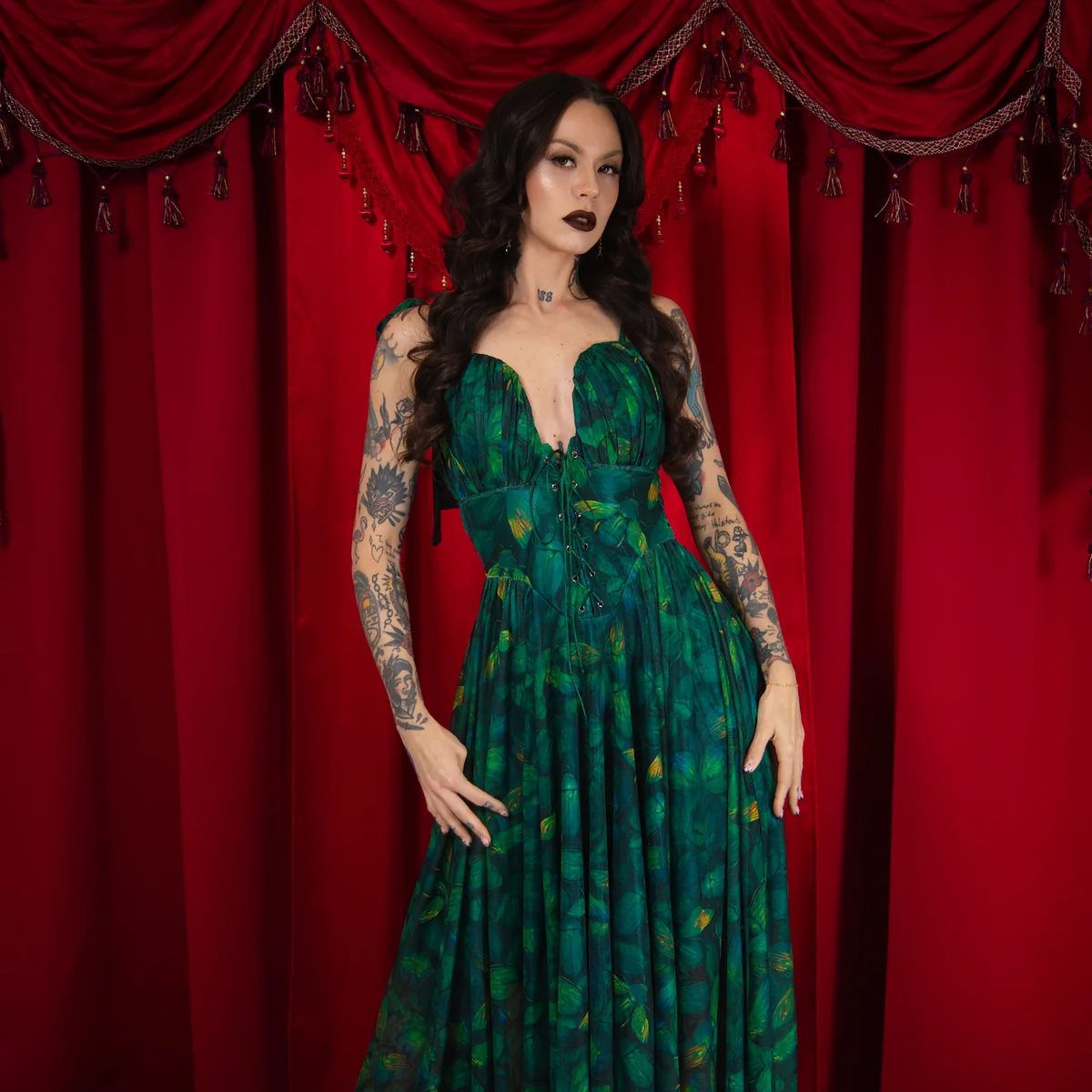 Woman in a green dress standing in front of red curtains with floral decorations.