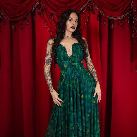 Woman in a green dress standing in front of red curtains with floral decorations.