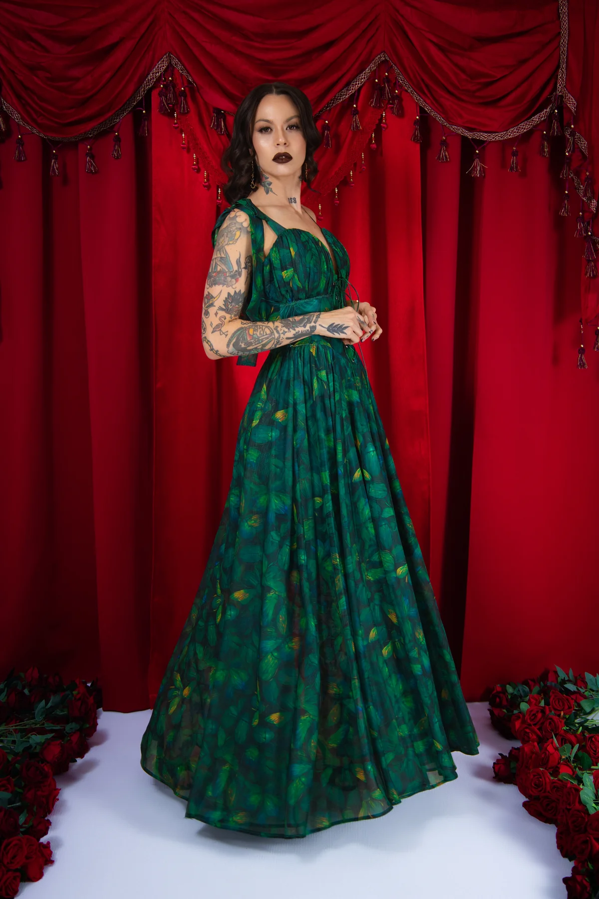 Woman in a green dress standing in front of red curtains with floral decorations.