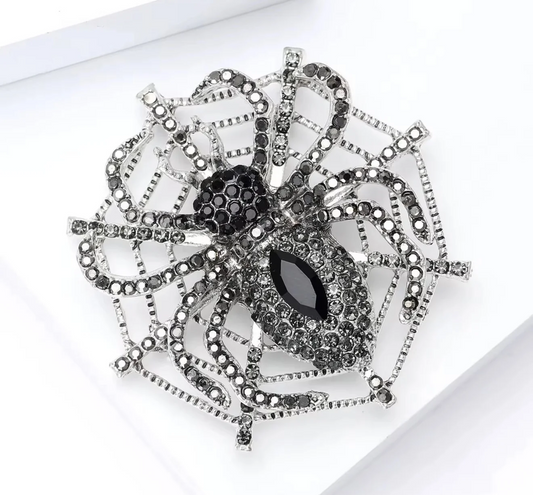 A large spider brooch featuring a black marquise-shaped center stone and black rhinestone-encrusted body, with silver-tone metal legs and web-like extensions adorned with small clear rhinestones, shown on a white background.