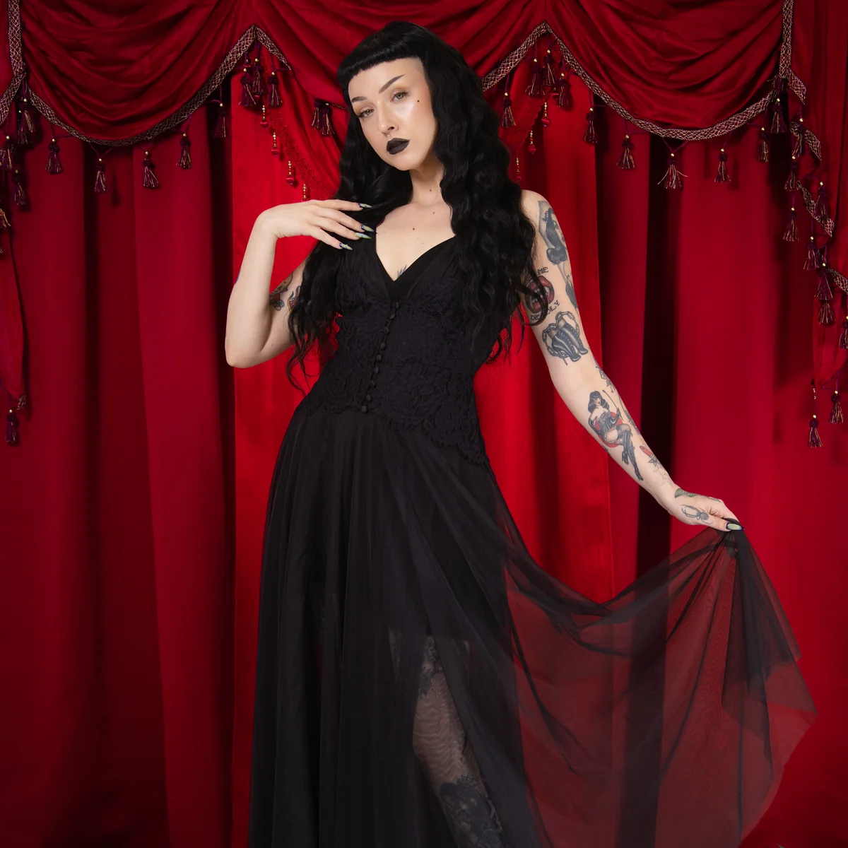 Woman in a black dress standing against a red curtain backdrop