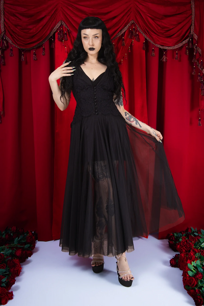 Woman in a black dress with sheer overlay against a red curtain backdrop