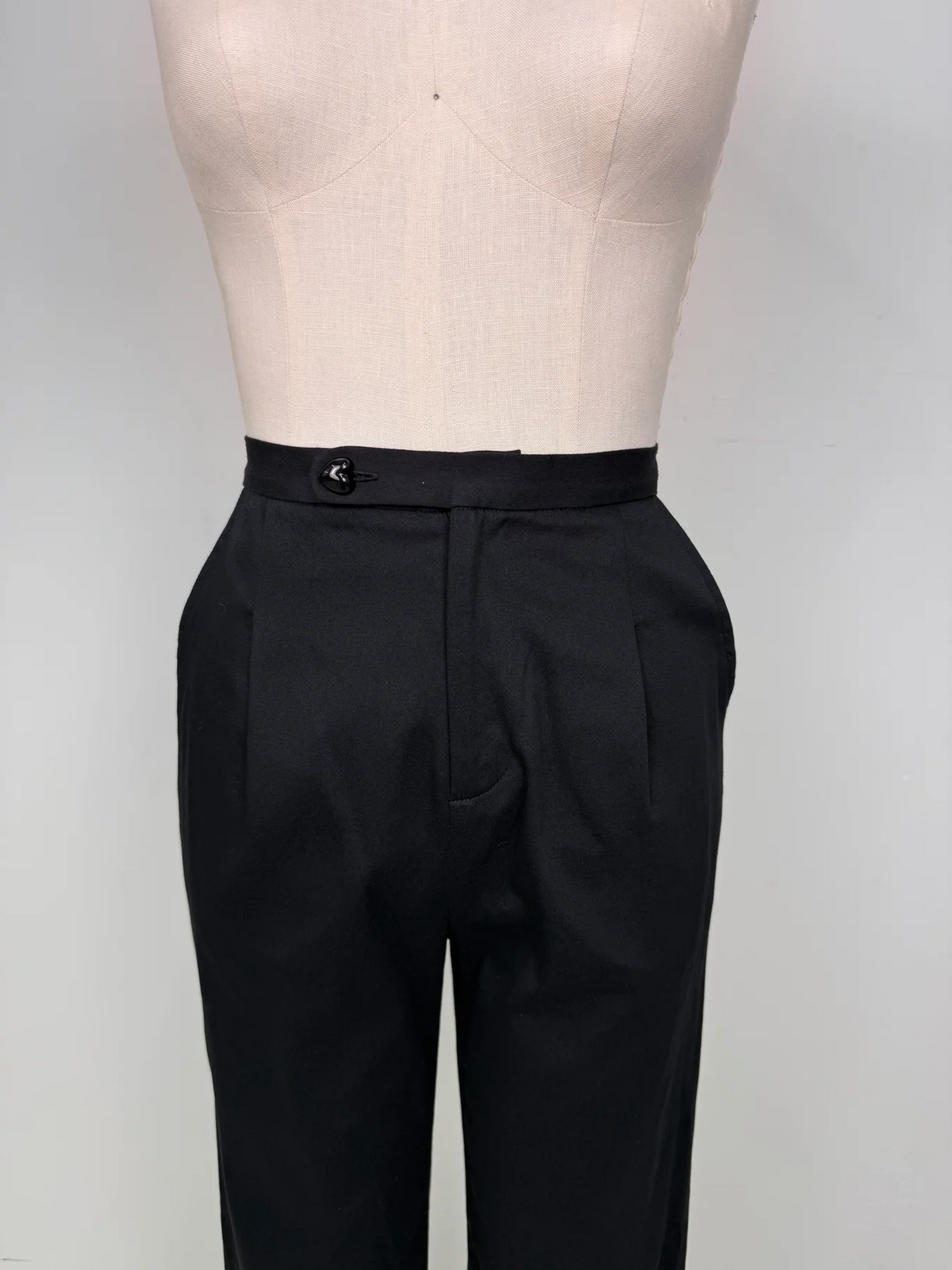 Black tailored trousers displayed on a cream dress form against a light gray studio background.
