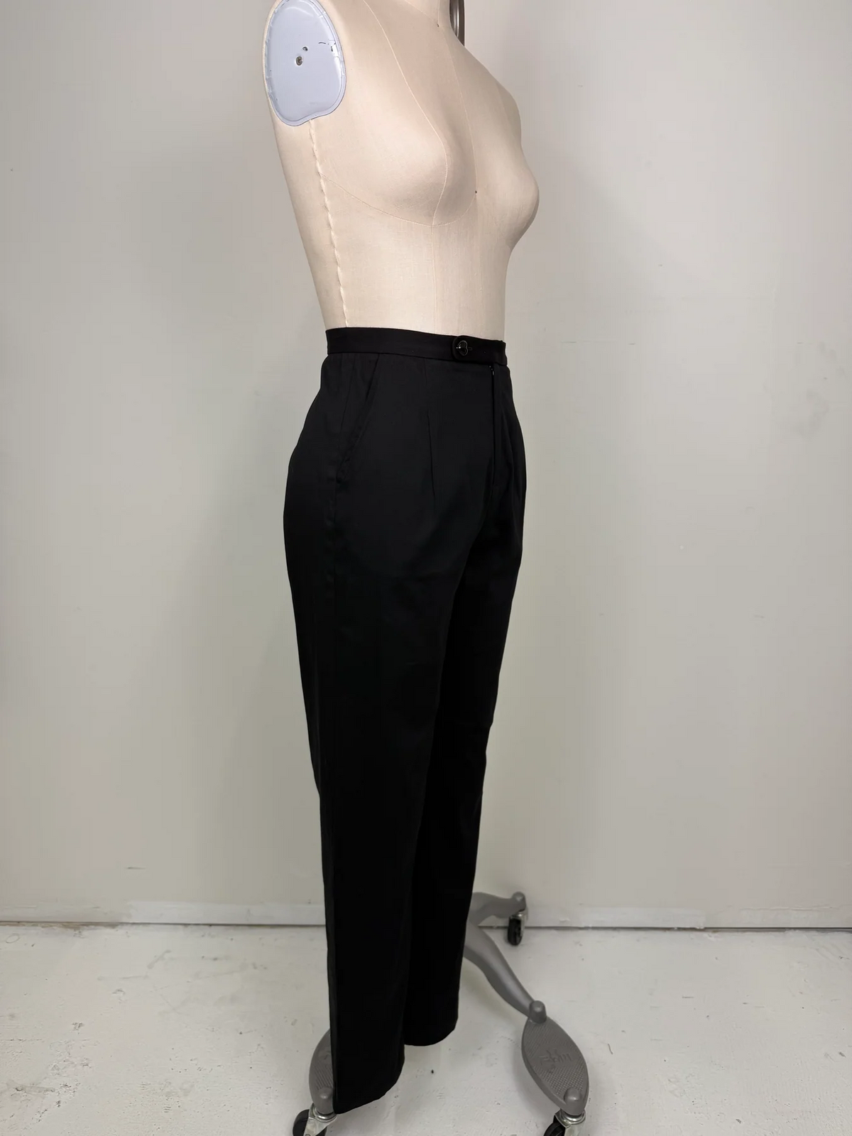 Black high-waisted tailored trousers displayed on a beige mannequin torso against a plain light gray wall.