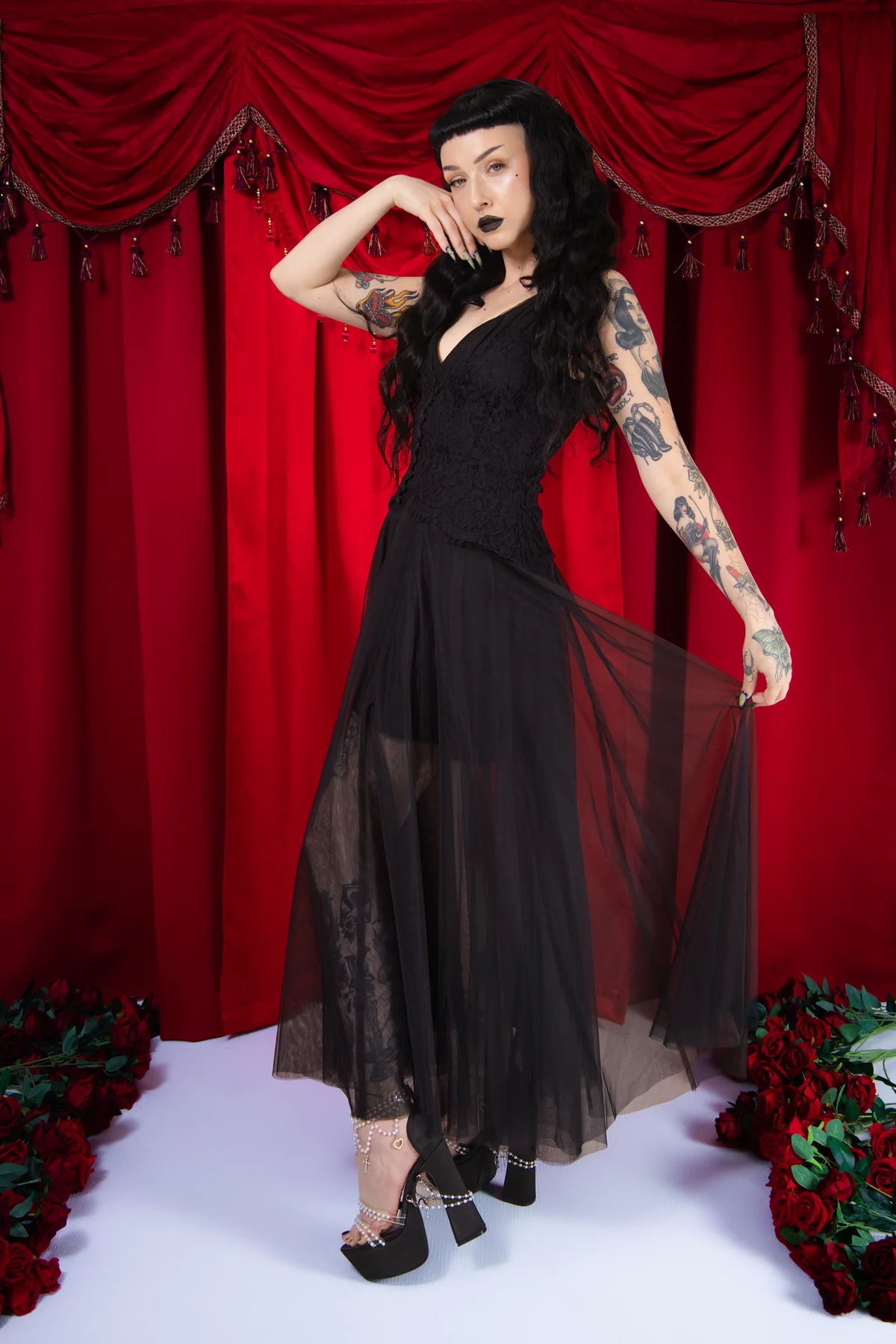 Woman in a black dress with sheer overlay against a red curtain backdrop