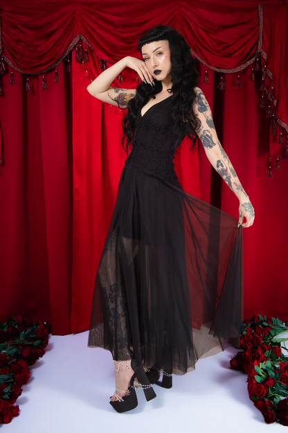 Woman in a black dress with sheer overlay against a red curtain backdrop