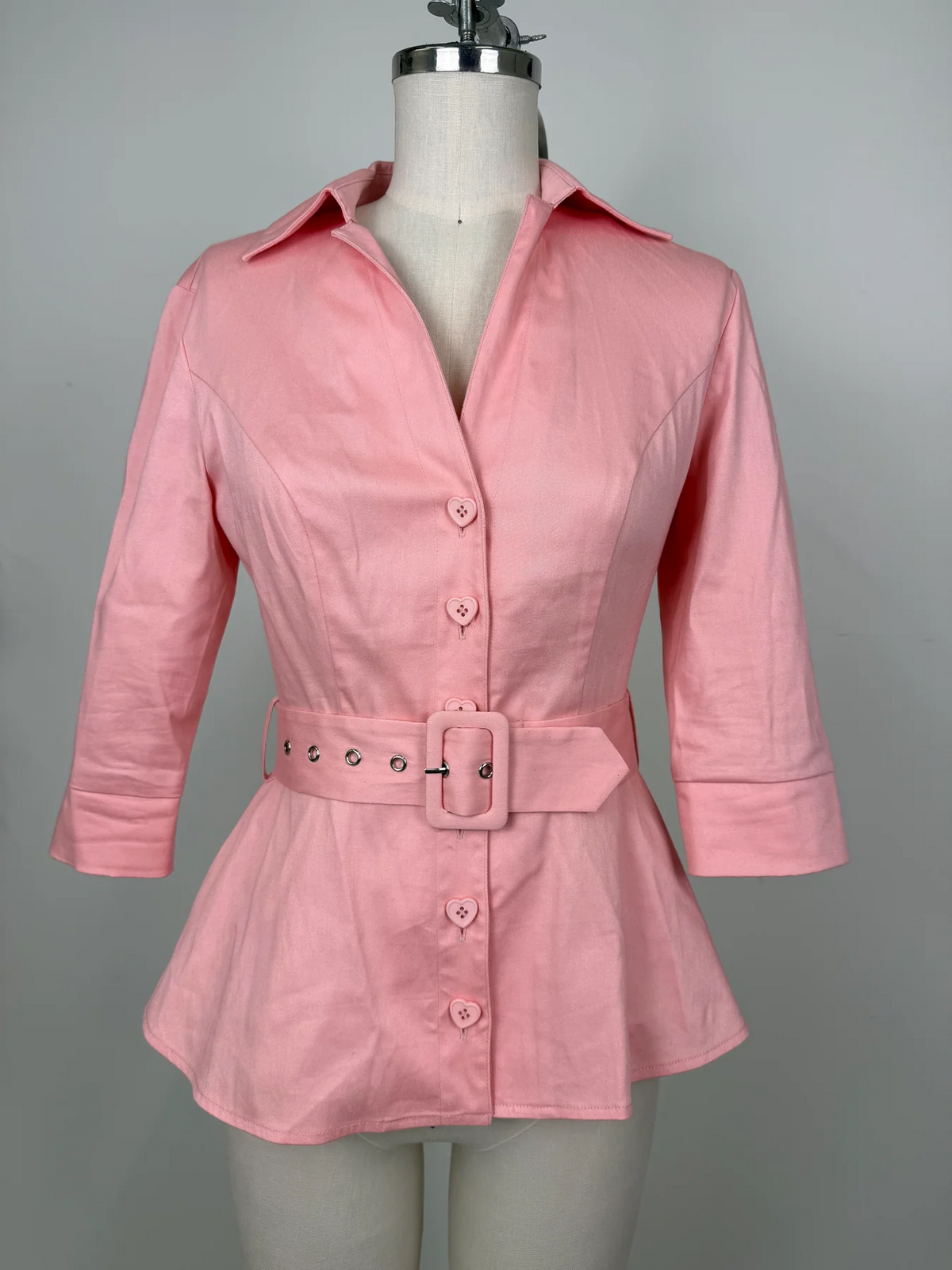 A pink long-sleeve button-front blouse with a matching belt and large square buckle, displayed on a mannequin torso against a plain light gray background.
