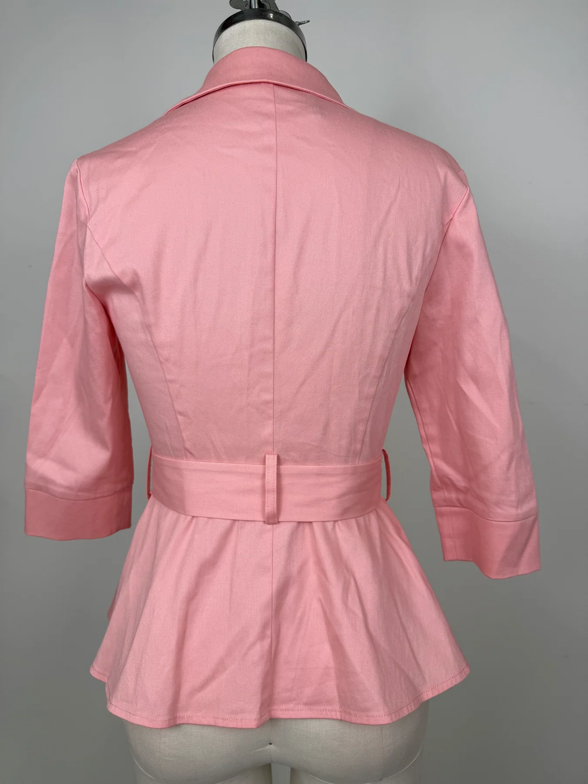 A pink women's blazer or jacket shown from the back on a dress form mannequin, featuring a collar, three-quarter sleeves, and a matching waist belt with a tie closure.