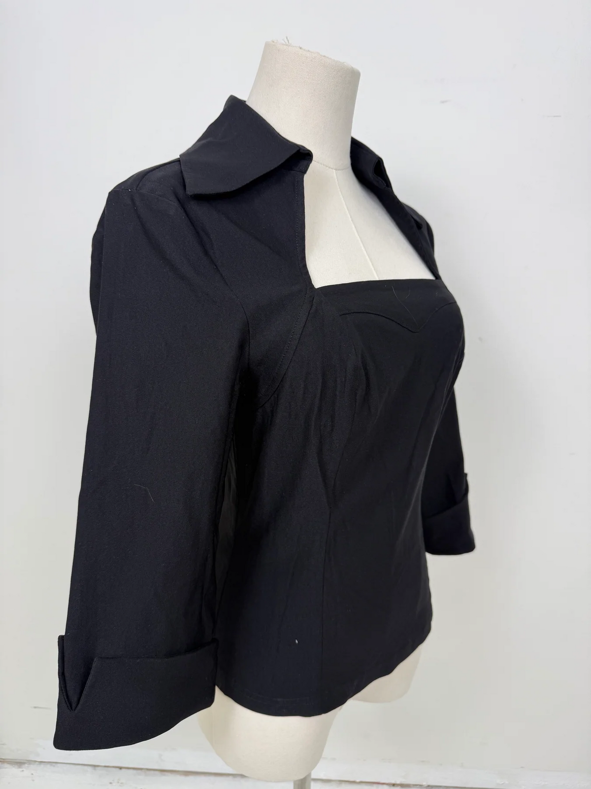 A black women's blouse with a square neckline, three-quarter sleeves, and cuffed sleeves, displayed on a cream mannequin torso against a white background.