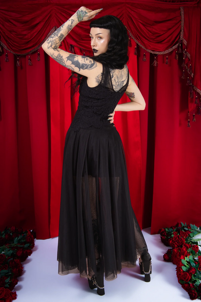 Woman in a black dress posing in front of red curtains with floral decorations.