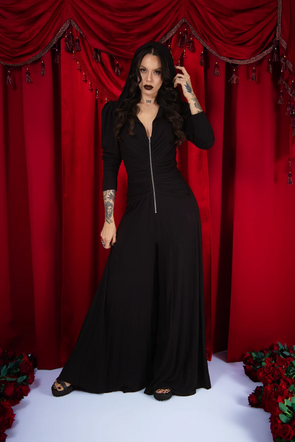 Woman in a black outfit standing in front of red curtains with floral decorations.