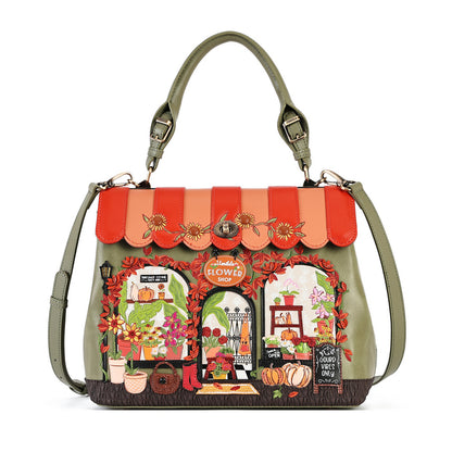 An olive green handbag with a detailed autumn-themed storefront patchwork design on the front, featuring orange and red striped awning details and floral patterns, shown on a plain white background.
