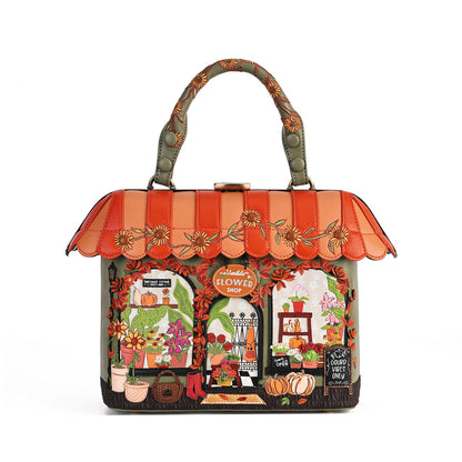 A decorative handbag designed to look like a storefront, featuring a scalloped orange and peach awning with floral embroidery, a top handle, and a detailed autumn-themed facade with pumpkins, flowers, and a chalkboard sign.