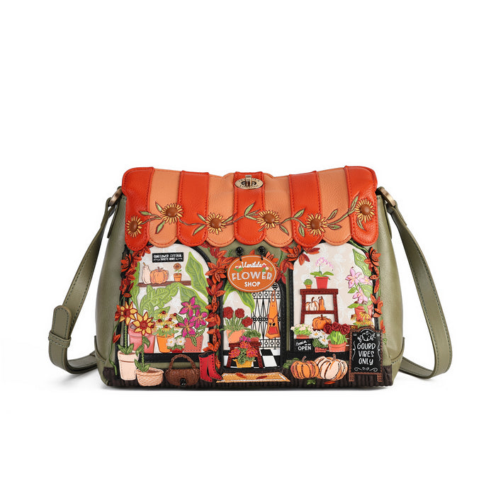 A shoulder bag with a green base and a highly detailed, colorful autumn-themed storefront illustration on the front. The top features a scalloped orange and red pattern with embroidered sunflower details.